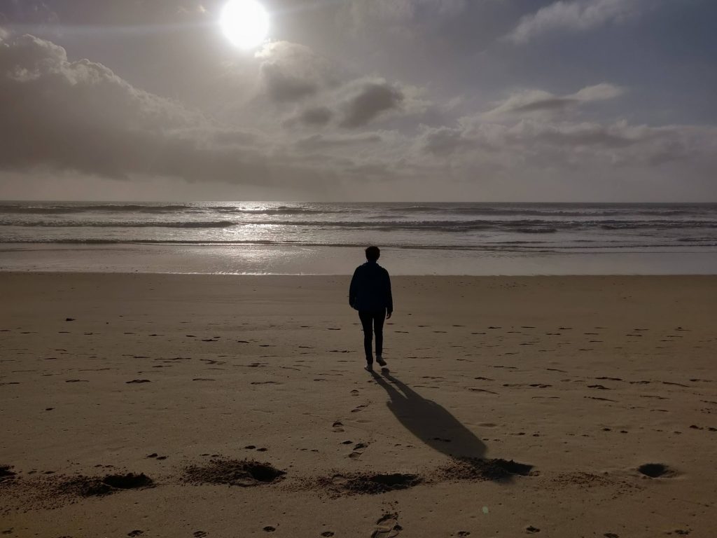 Person walking on a beach looking out to a calm sea