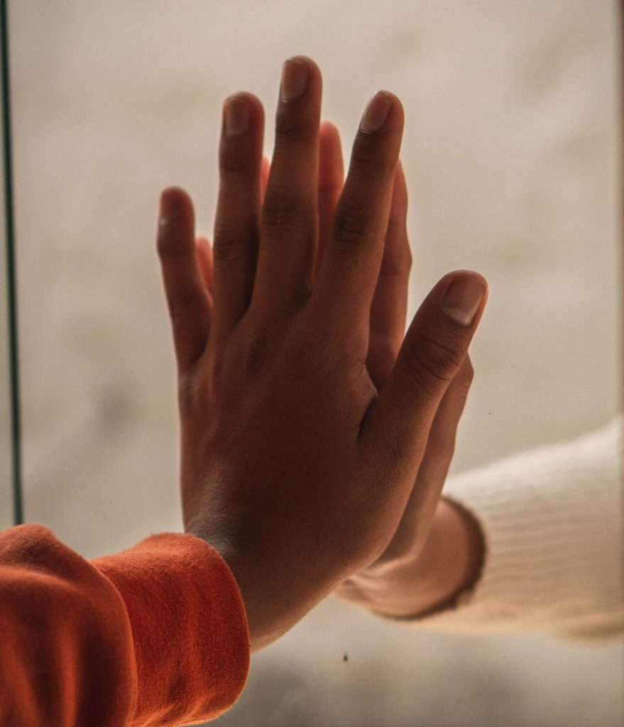 Survivor Syndrome: Building Bridges and meeting people where they are. Two hands, one on either side of a pane of glass in a window