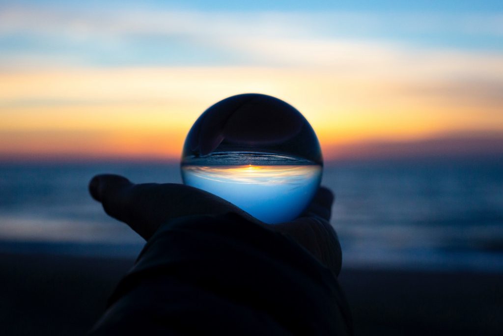 Back to the Future: Scenario Planning with Agility. Image of a hand holding a glass ball reflecting a sunset horizon